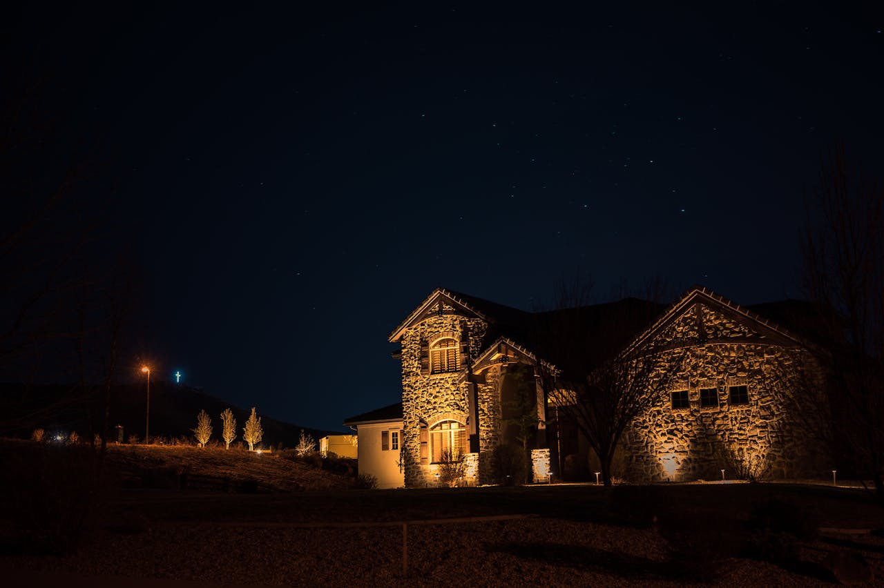 A beautifully lit stone mansion stands under a star-filled night sky, exuding a serene and mystical charm.