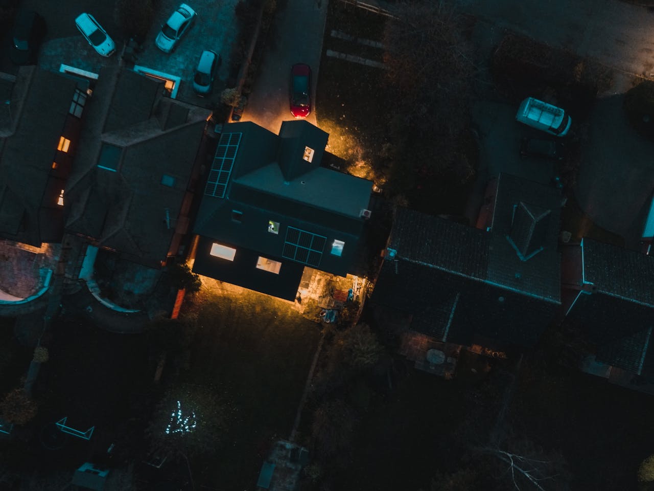 A captivating aerial view of a suburban neighborhood at night with cars and houses illuminated.